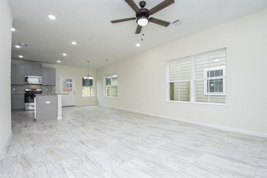 Spacious, empty room with modern kitchen, marble-like tiled flooring, recessed lighting, ceiling fan, and large windows allowing natural light.