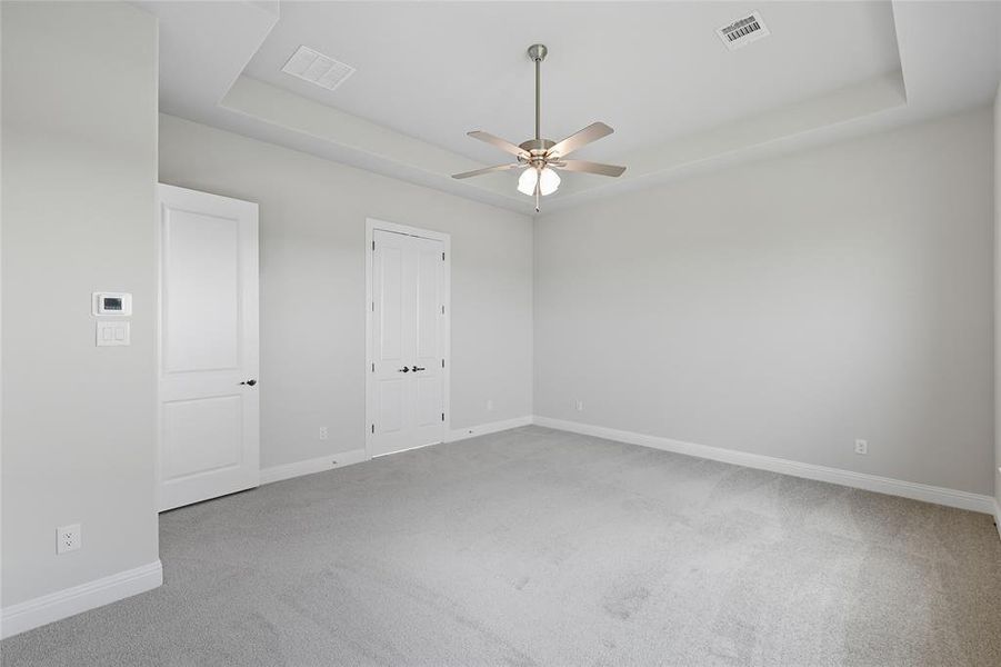 Spare room featuring a raised ceiling, light colored carpet, and a ceiling fan Spare room featuring a raised ceiling, light colored carpet, and a ceiling fan