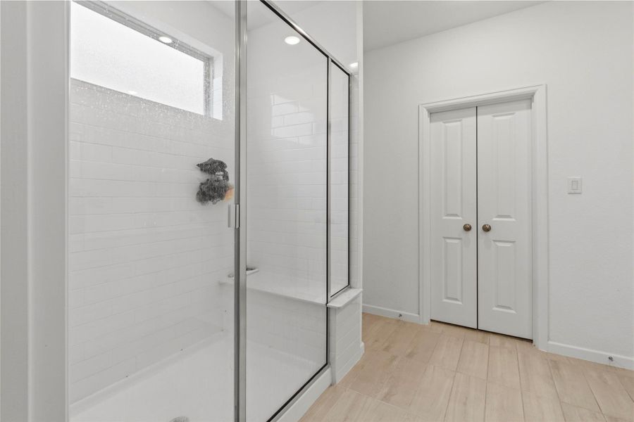 Sleek and modern bathroom off the primary with elegant white tiles, complemented by stylish wood-look flooring and convenient double doors for storage. Sleek and modern bathroom off the primary with elegant white tiles, complemented by stylish wood-look flooring and convenient double doors for storage.