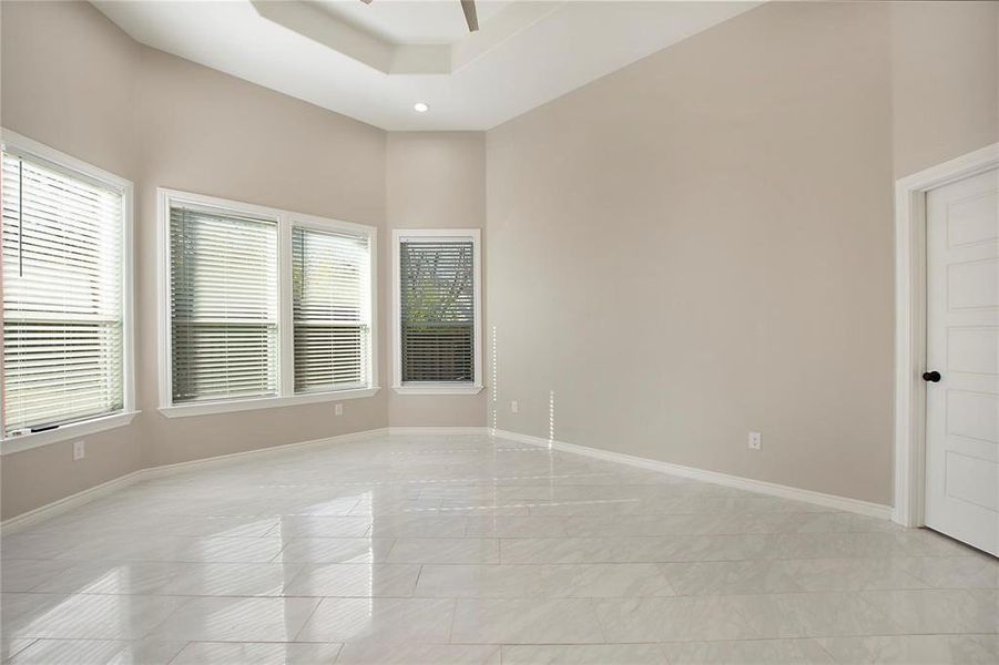 Unfurnished room with a ceiling fan, a towering ceiling, light tile patterned floors, and a tray ceiling Unfurnished room with a ceiling fan, a towering ceiling, light tile patterned floors, and a tray ceiling