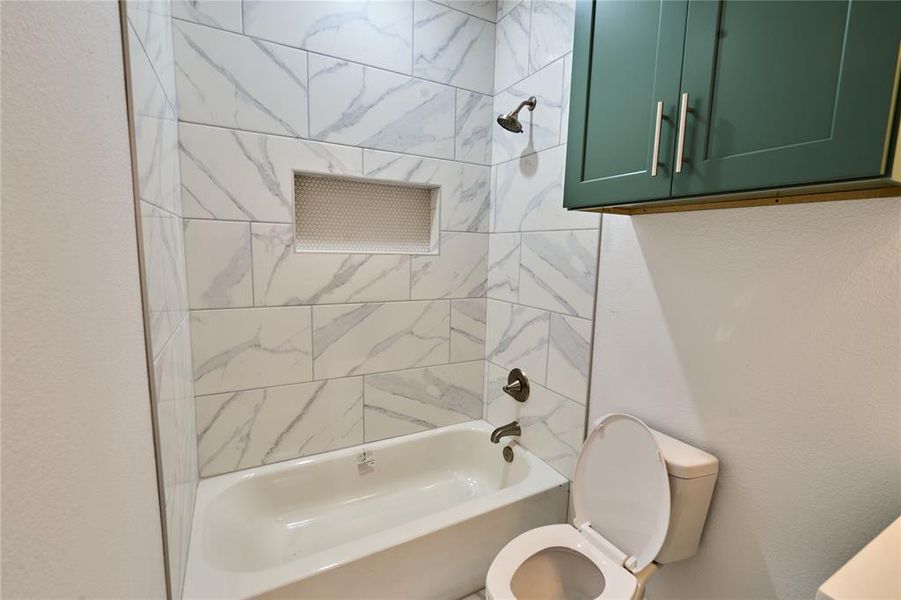 Bathroom featuring a bathtub with subway tile surround, recessed shower niche, oil-rubbed bronze shower fixtures, and green wall cabinetry with silver hardware