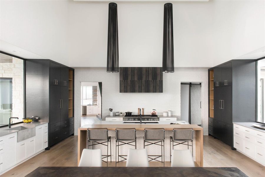 Kitchen with light wood-style floors, open shelves, light stone counters, white cabinetry, and a towering ceiling