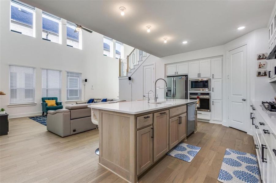 Dual tone kitchen featuring open floor plan, a center island with sink, light wood-type flooring, stainless steel appliances, and ceiling fan Dual tone kitchen featuring open floor plan, a center island with sink, light wood-type flooring, stainless steel appliances, and ceiling fan
