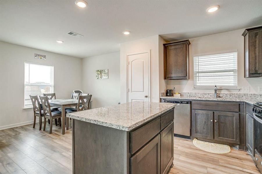 Kitchen featuring dark brown cabinets, a center island, light stone counters, plenty of natural light, and recessed lighting