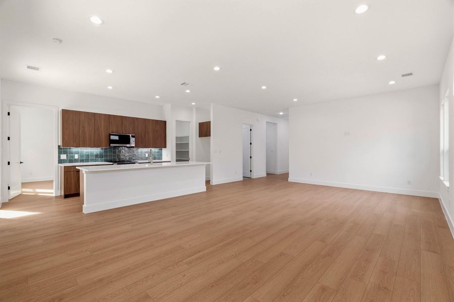 Kitchen featuring open floor plan, light countertops, an island with sink, decorative backsplash, and light wood-type flooring