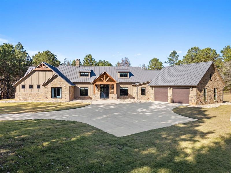 Modern farmhouse featuring stone siding, a metal roof, a front lawn, and driveway