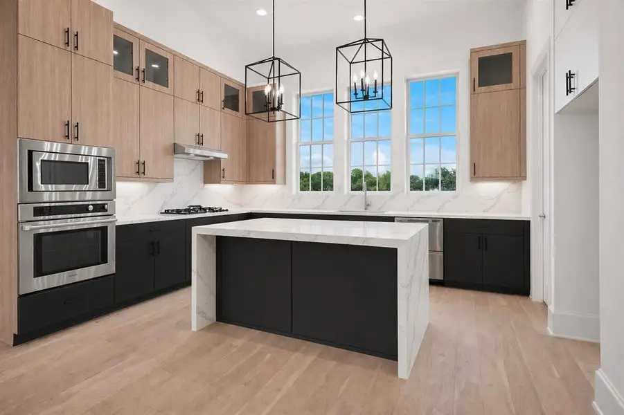 Contemporary kitchen featuring a waterfall island with a stone countertop, light wood-finish flooring, and a suite of stainless steel appliances