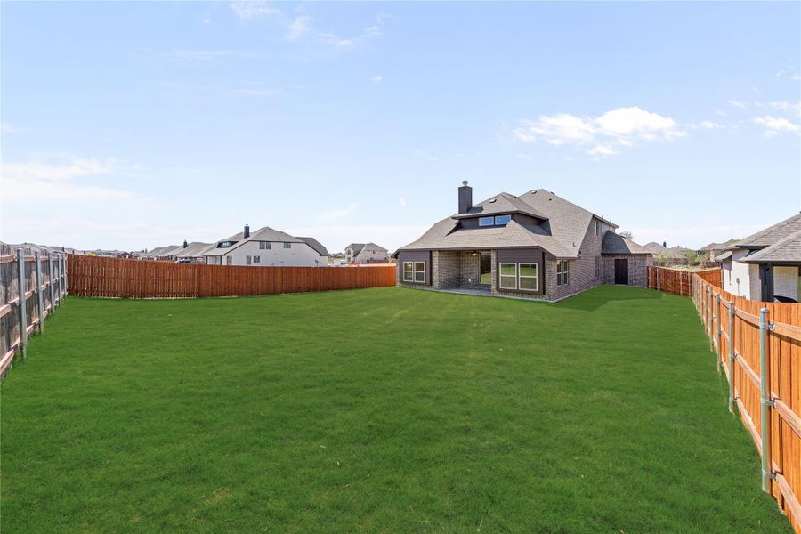Large backyard with green lawn, wood privacy fence, and brick home with covered patio in background Large backyard with green lawn, wood privacy fence, and brick home with covered patio in background