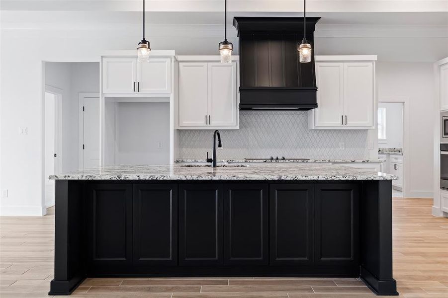 Kitchen featuring backsplash, custom exhaust hood, light hardwood / wood-style flooring, and light stone counters