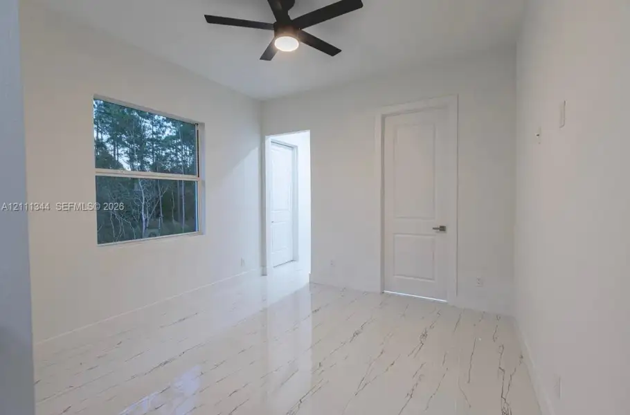 Neutral interior featuring polished stone-finish flooring, a matte black ceiling fan, and a single-hung window with exterior greenery Neutral interior featuring polished stone-finish flooring, a matte black ceiling fan, and a single-hung window with exterior greenery