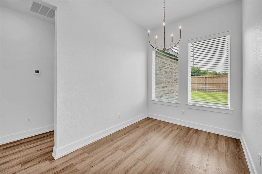Unfurnished dining area with an inviting chandelier, baseboards, wood finished floors, and visible vents Unfurnished dining area with an inviting chandelier, baseboards, wood finished floors, and visible vents