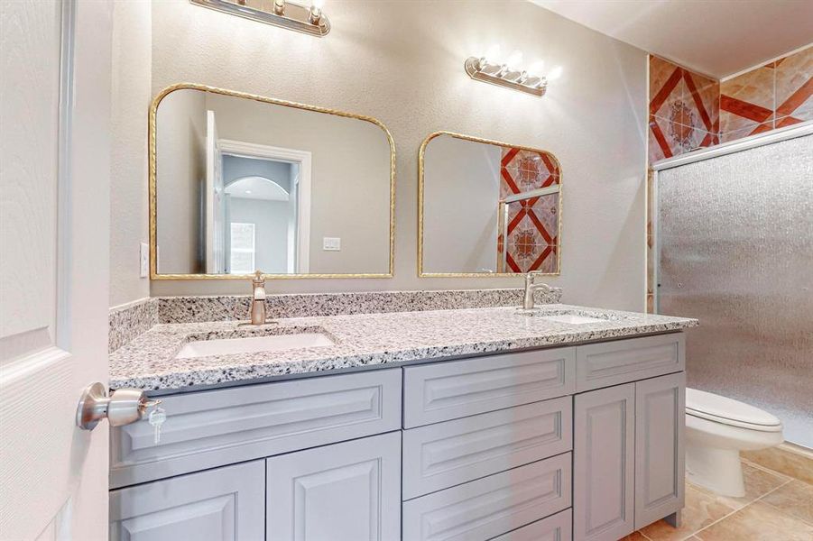 Bathroom with toilet, dual vanity, and tile flooring