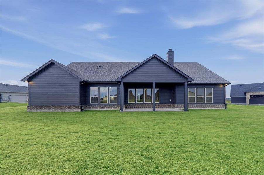 Expansive green lawn bordering the rear elevation featuring dark siding and a covered patio Expansive green lawn bordering the rear elevation featuring dark siding and a covered patio