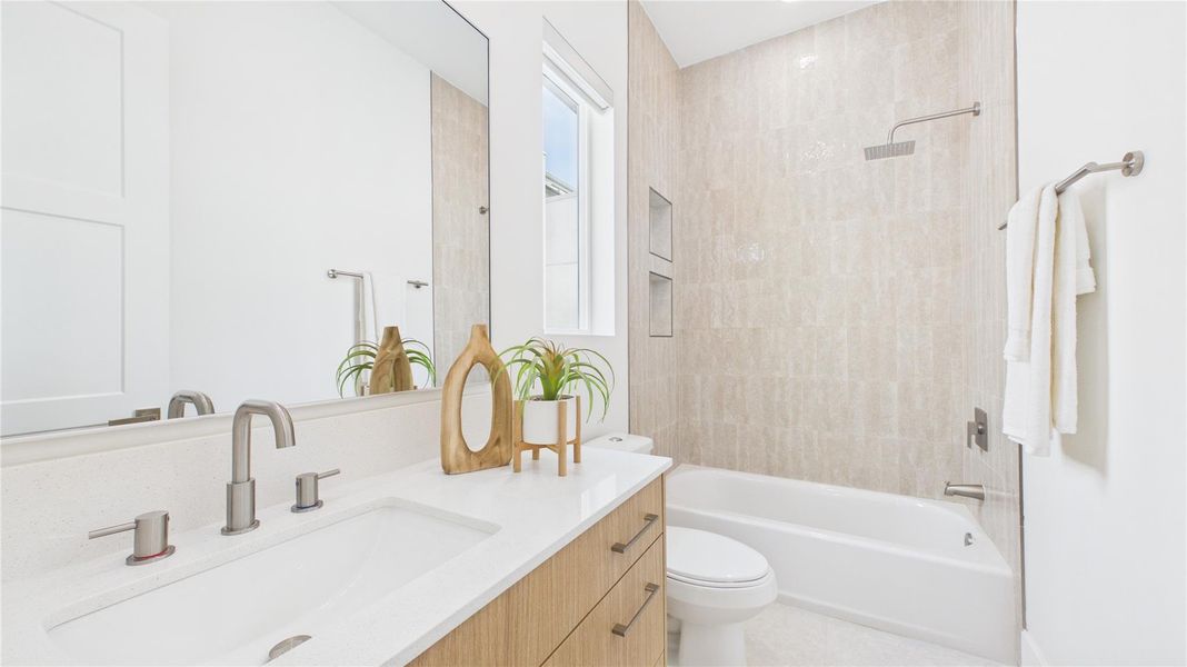 This modern bathroom features a sleek design with a dual sink vanity, contemporary fixtures, a large mirror, and a bathtub with a rainfall showerhead. Neutral tones and natural light enhance the clean, spacious feel.