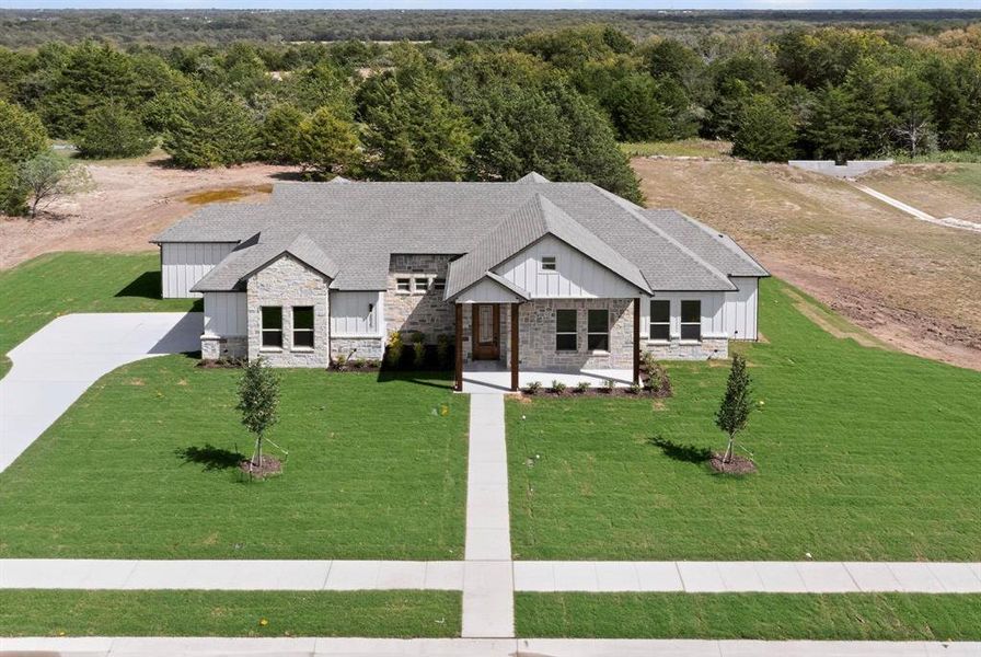 View of front of house with board and batten siding, stone siding, a shingled roof, covered porch, and a wooded view