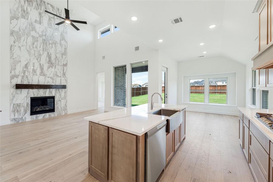 Open kitchen with center island, wood cabinets, and marble tile fireplace wall in adjoining living area with high ceilings