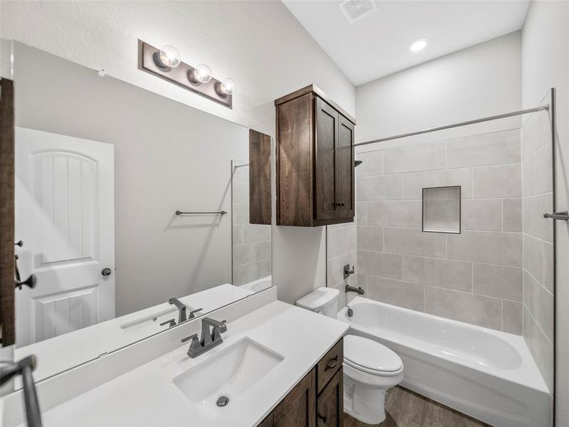 Bathroom with visible vents, toilet, vanity, wood finished floors, and shower / tub combination Bathroom with visible vents, toilet, vanity, wood finished floors, and shower / tub combination