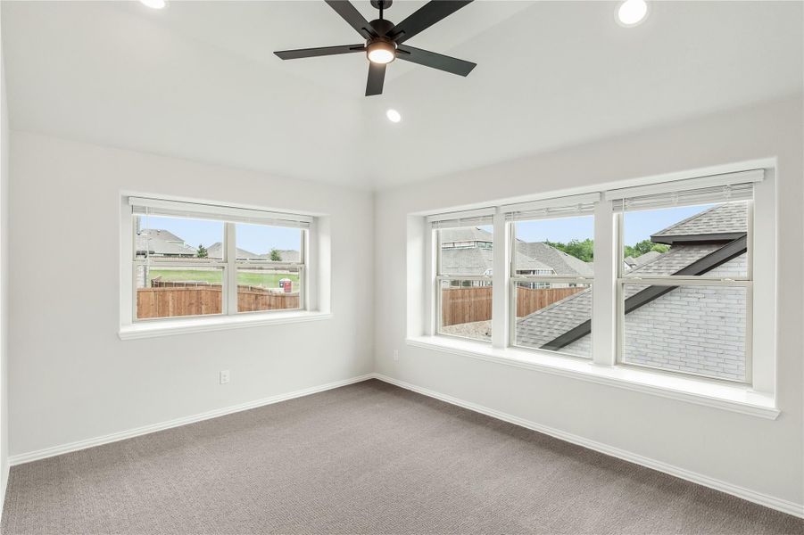 Empty bedroom with carpet, ceiling fan, and large windows overlooking neighborhood rooftops Empty bedroom with carpet, ceiling fan, and large windows overlooking neighborhood rooftops
