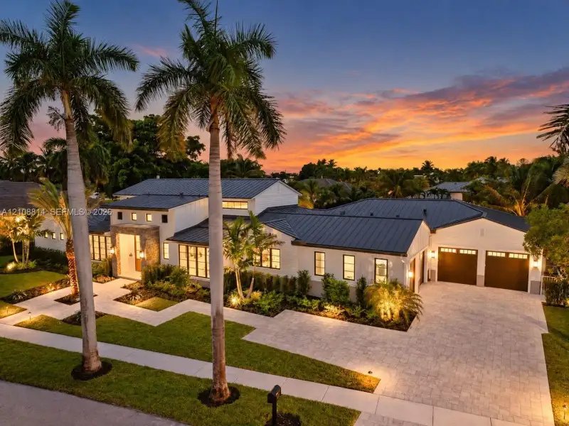 Modern architectural exterior featuring a metal roof, stone facade accents, multi-pane windows, and a paved driveway leading to an attached two-car garage Modern architectural exterior featuring a metal roof, stone facade accents, multi-pane windows, and a paved driveway leading to an attached two-car garage