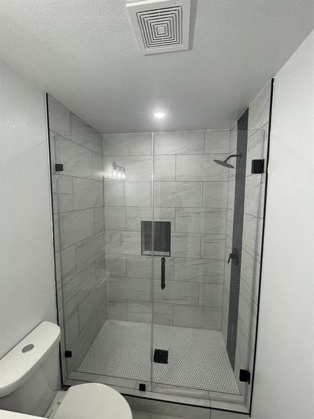 Bathroom with a shower with door, a textured ceiling, and toilet