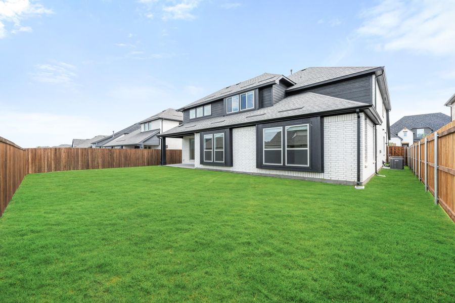 Backyard of two-story home with white brick exterior, dark trim, green lawn, and wood privacy fence.