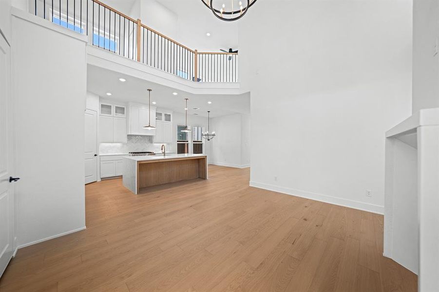 Unfurnished living room featuring a chandelier, light wood finished floors, a high ceiling, and recessed lighting