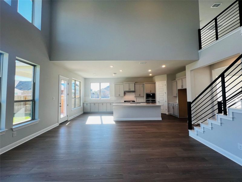 Unfurnished living room with a towering ceiling, healthy amount of natural light, stairs, dark wood-style flooring, and recessed lighting