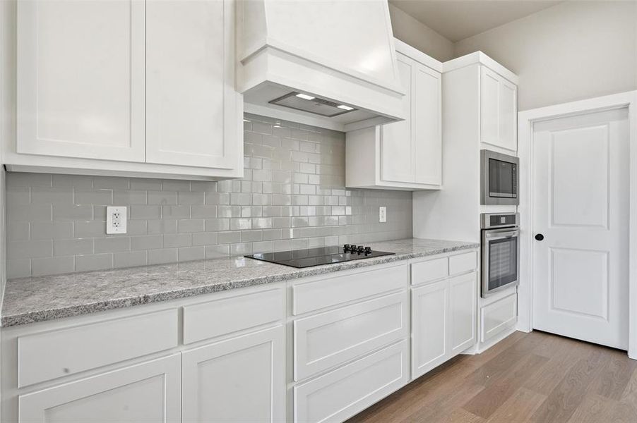 Kitchen with white cabinetry, light stone counters, stainless steel appliances, light wood-style floors, and tasteful backsplash
