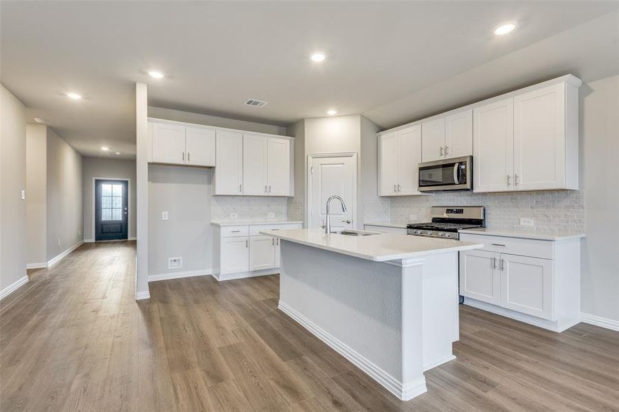 Kitchen with white cabinets, stainless steel appliances, a center island with sink, dark wood-style floors, and recessed lighting