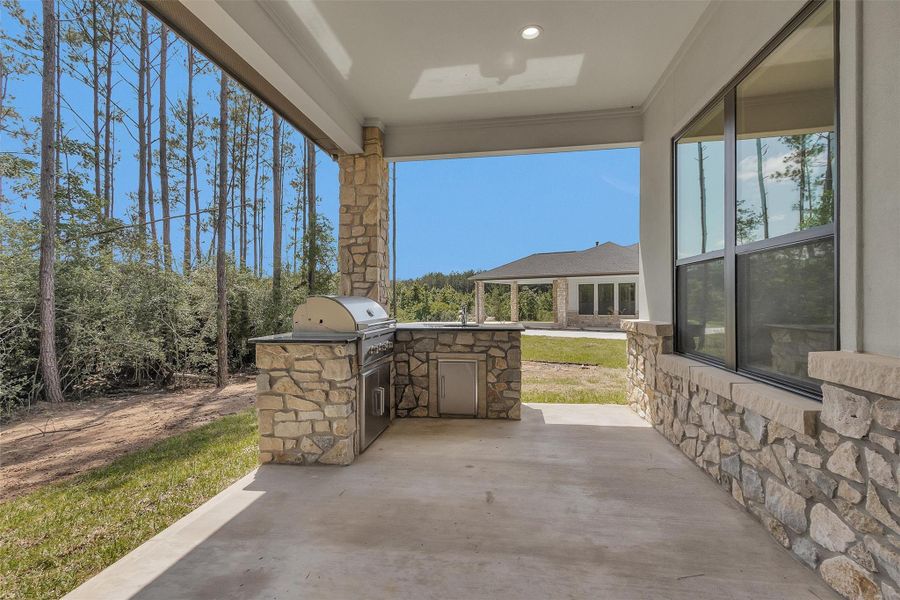Surrounded by trees and set against a backdrop of both privacy and space, the covered outdoor kitchen is outfitted with a built-in grill, sink, stonework accents, and ample prep space for entertaining. Surrounded by trees and set against a backdrop of both privacy and space, the covered outdoor kitchen is outfitted with a built-in grill, sink, stonework accents, and ample prep space for entertaining.
