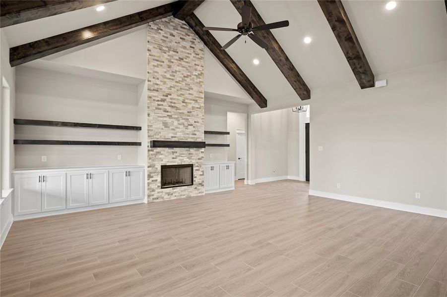 Unfurnished living room with a fireplace, light wood-style flooring, beamed ceiling, a ceiling fan, and high vaulted ceiling