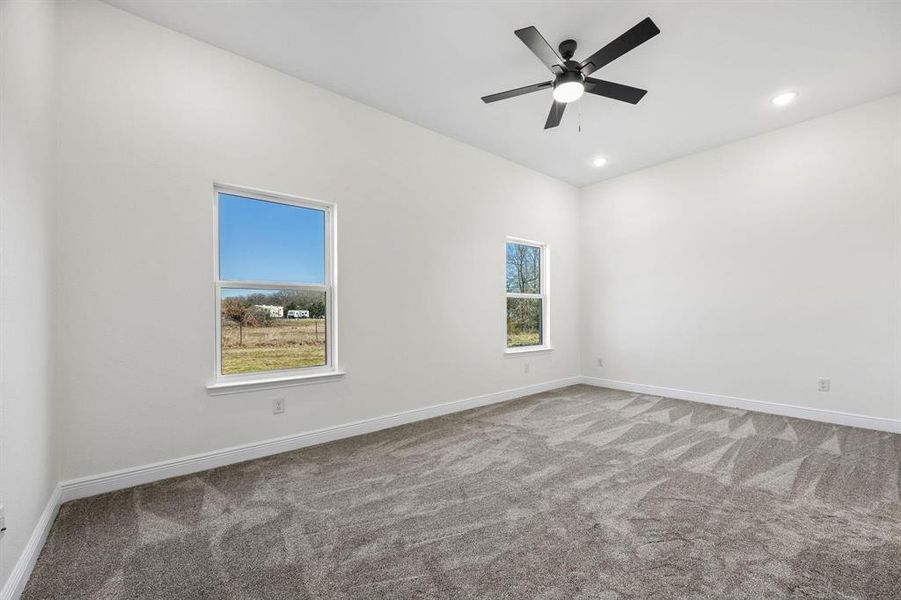 Spacious room featuring neutral carpeting, two windows, recessed lighting, a modern ceiling fan, and white walls Spacious room featuring neutral carpeting, two windows, recessed lighting, a modern ceiling fan, and white walls