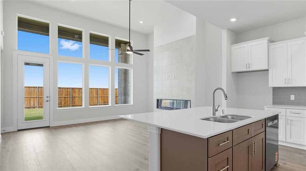 Kitchen with two tone cabinetry, a center island with sink, light wood finished floors, light stone counters, and tasteful backsplash