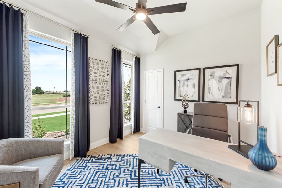 Home office with vaulted ceiling, ceiling fan, large windows, and a desk with blue patterned rug