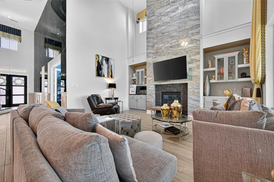 This living room features a spacious, open design with high ceilings and abundant natural light. It includes a modern fireplace with a sleek stone finish, built-in shelving, and a large TV mounted above. The room is elegantly furnished with plush seating, a stylish glass coffee table, and tasteful decor accents. This living room features a spacious, open design with high ceilings and abundant natural light. It includes a modern fireplace with a sleek stone finish, built-in shelving, and a large TV mounted above. The room is elegantly furnished with plush seating, a stylish glass coffee table, and tasteful decor accents.