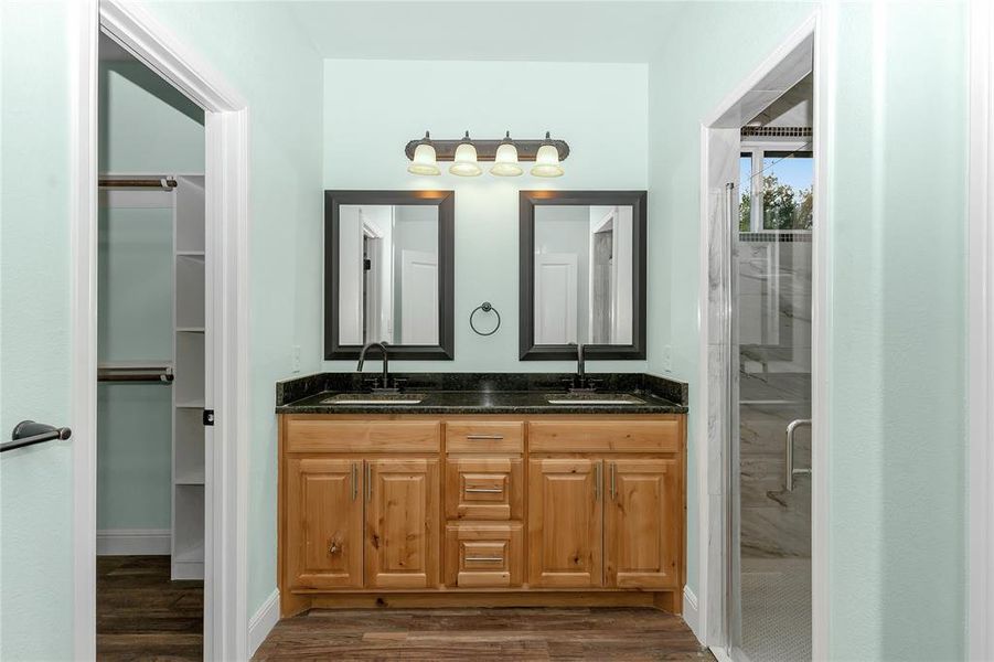 Bathroom featuring double vanity, a shower stall, dark wood finished floors, and a spacious closet