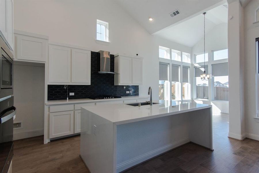 Kitchen featuring a healthy amount of sunlight, wall chimney range hood, sink, and high vaulted ceiling