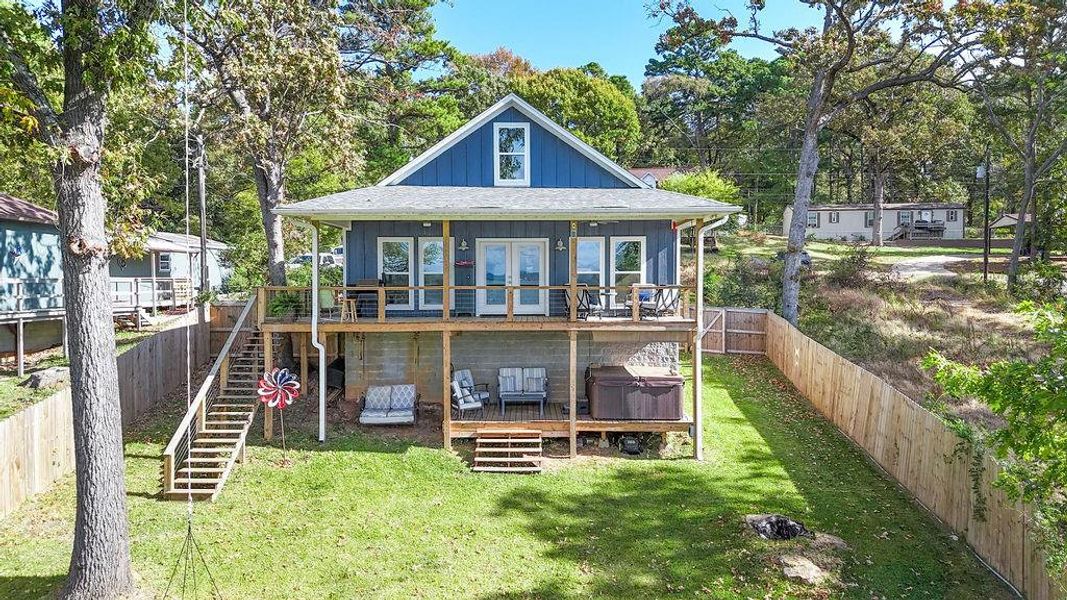 Back of property with a deck, a hot tub, board and batten siding, stairway, and a fenced backyard