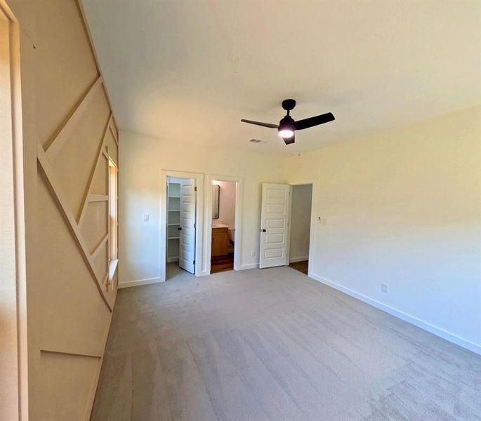 Unfurnished bedroom featuring connected bathroom, a walk in closet, carpet, and a ceiling fan Unfurnished bedroom featuring connected bathroom, a walk in closet, carpet, and a ceiling fan