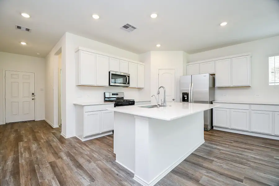 Discover a modern kitchen with sleek white cabinetry, stainless steel appliances, and a spacious island with a sink. Its open layout and abundant natural light make it truly inviting, while elegant wood flooring adds a touch of warmth.