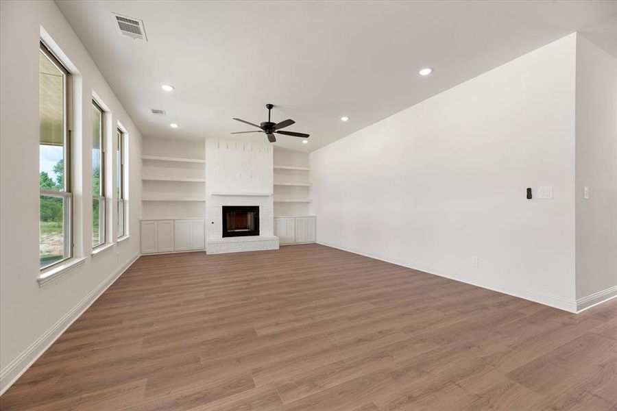 Unfurnished living room with built in shelves, ceiling fan, hardwood / wood-style floors, and a fireplace