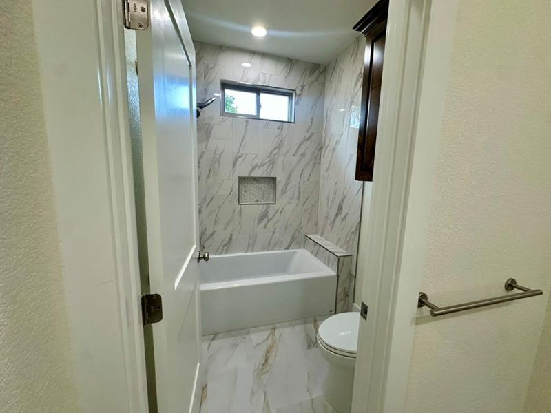 Full bath featuring a textured wall, marble look tiles, and bathing tub / shower combination