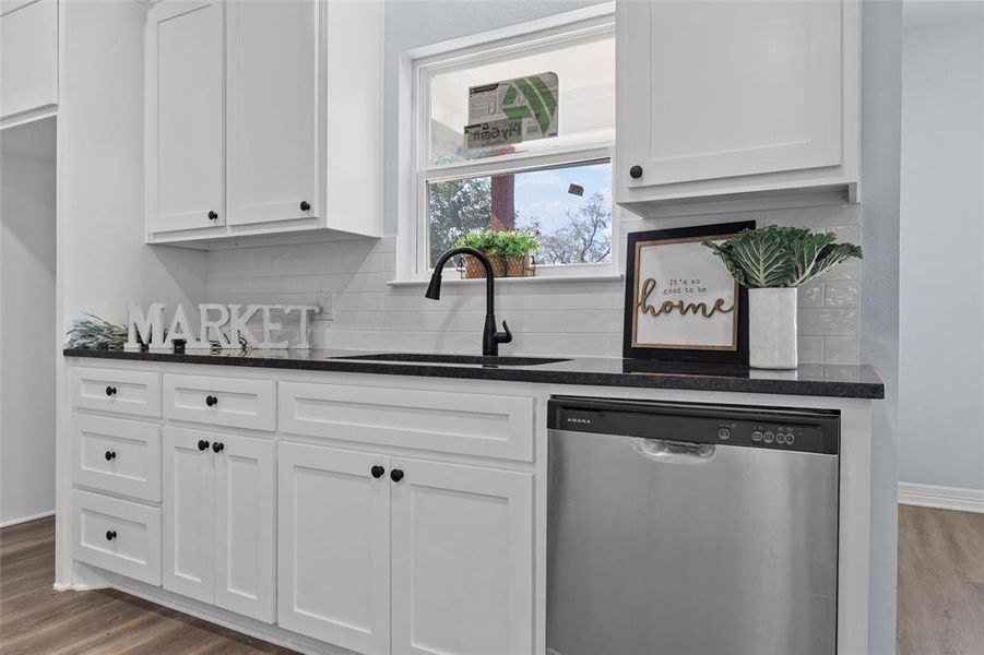 Kitchen with dark wood-style flooring, stainless steel dishwasher, white cabinetry, and dark stone counters