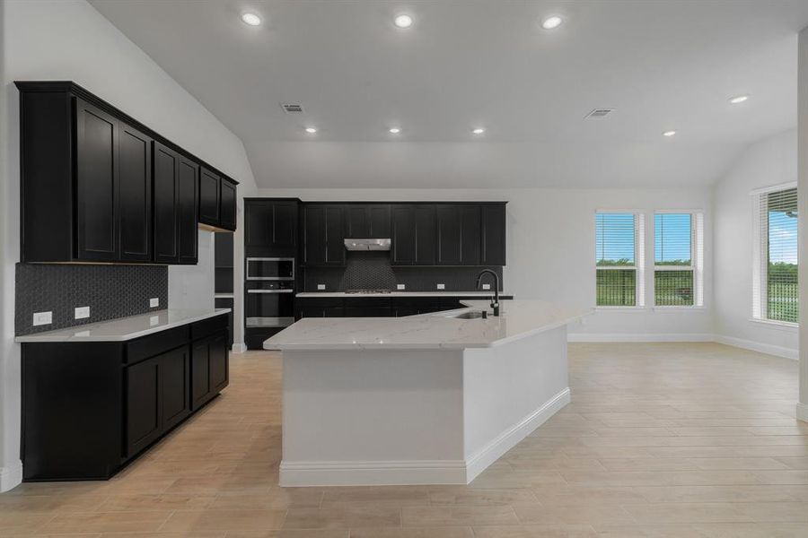 Kitchen with a center island with sink, vaulted ceiling, and tasteful backsplash