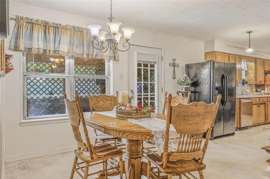 Dining area featuring an overhead chandelier, two windows with lattice-patterned screens, and an adjacent kitchen with wood cabinetry and stainless steel appliances Dining area featuring an overhead chandelier, two windows with lattice-patterned screens, and an adjacent kitchen with wood cabinetry and stainless steel appliances