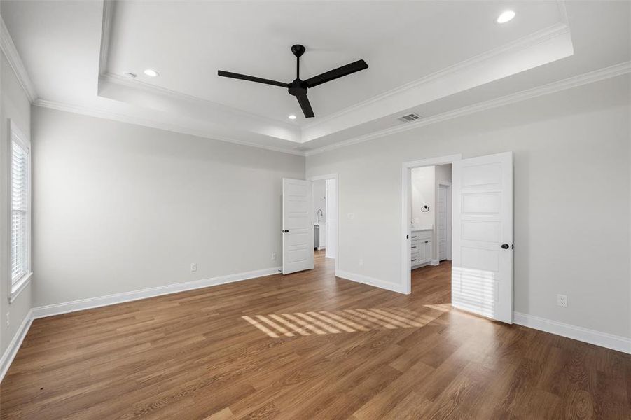 Unfurnished bedroom featuring a raised ceiling, wood finished floors, crown molding, ceiling fan, and recessed lighting Unfurnished bedroom featuring a raised ceiling, wood finished floors, crown molding, ceiling fan, and recessed lighting