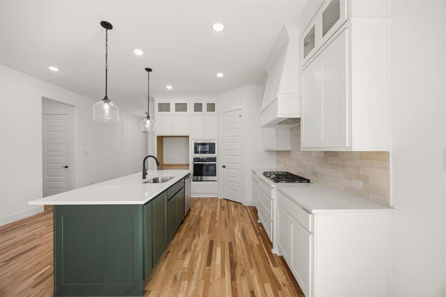 Kitchen featuring dual tone cabinetry, glass insert cabinets, an island with sink, light wood-style floors, and stainless steel appliances