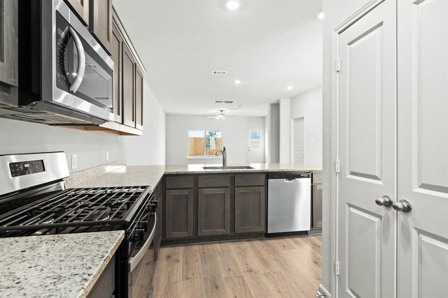 Kitchen featuring stainless steel appliances, light wood-style floors, dark brown cabinets, light stone counters, and recessed lighting Kitchen featuring stainless steel appliances, light wood-style floors, dark brown cabinets, light stone counters, and recessed lighting