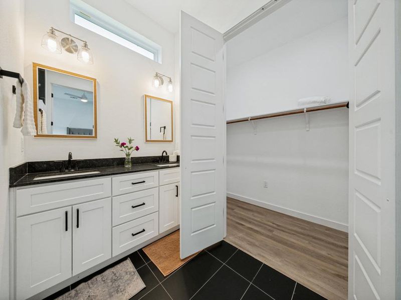 Double vanity with sleek black countertops and mirrors offers convenience adjacent to a spacious walk-in closet. Double vanity with sleek black countertops and mirrors offers convenience adjacent to a spacious walk-in closet.