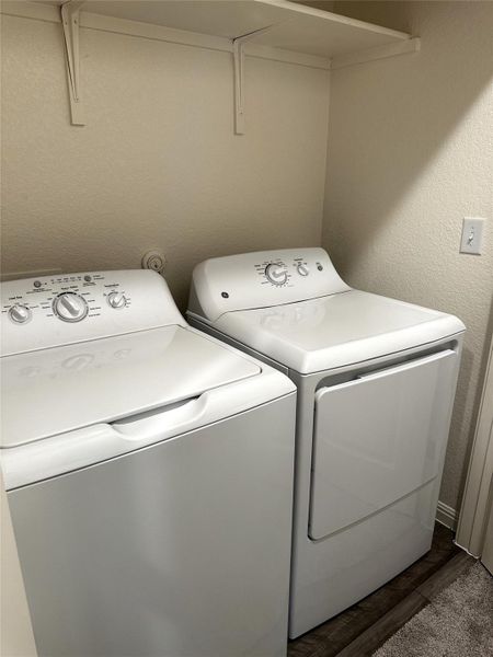 Clothes washing area featuring a textured wall, laundry area, washing machine and dryer, and dark wood finished floors. Washer and dryer convey with property.